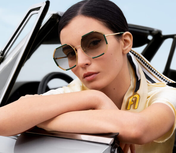 Jeune femme brune au volant d'une voiture, portant des lunettes Furla en métal doré et vert, avec un foulard dans les cheveux