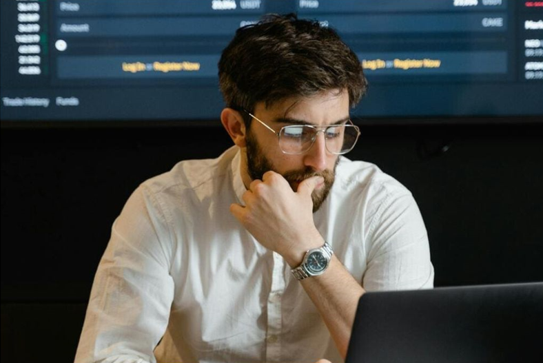 Jeune homme brun et barbu devant un ordinateur, illustrant les verres mi-distance Nikon