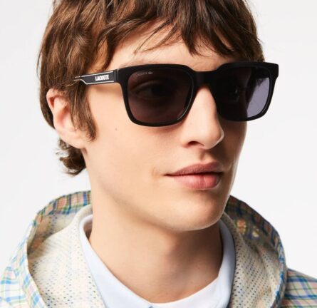 Jeune homme brun portant des lunettes de soleil Lacoste avec le logo Lacoste sur la branche
