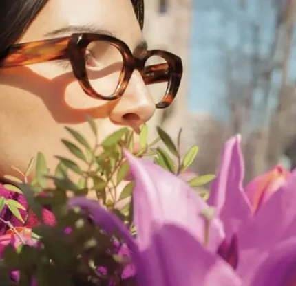 Femme brune portant des lunettes Lafont en acétate écaille, tenant un bouquet de lys violets, en extérieur sous une lumière douce de fin d’hiver.