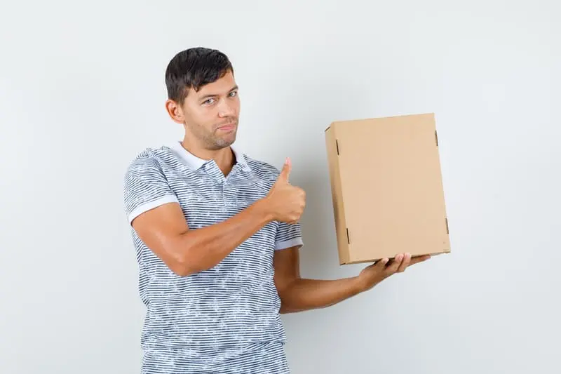 Jeune homme souriant tenant un colis et levant le pouce – service de livraison à domicile VISION BORDELAISE